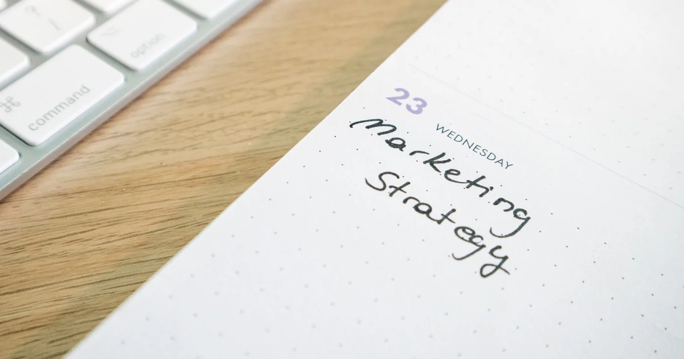 A planner with the words Marketing Strategy on a desk with a keyboard